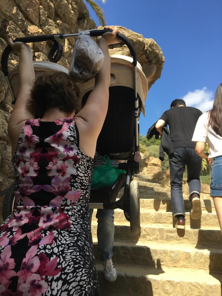 Turistipariskunta kantamassa tuplarattaita ylös Park Güellin portaita
